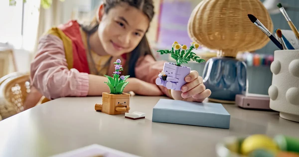 A girl at a white table smiling next to the finished LEGO Cozy Plants, a brown pot and a purple pot with plants