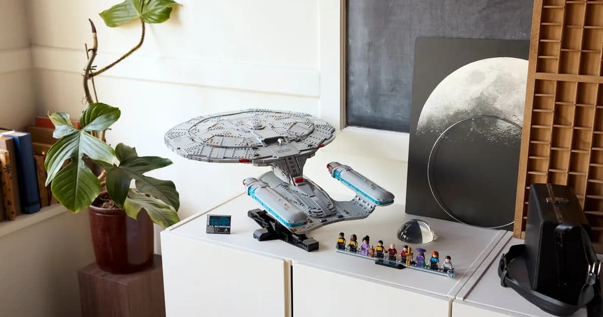 LEGO Star Trek Enterprise-D on its black stand on a white sideboard, nine crew minifigures lined up in front