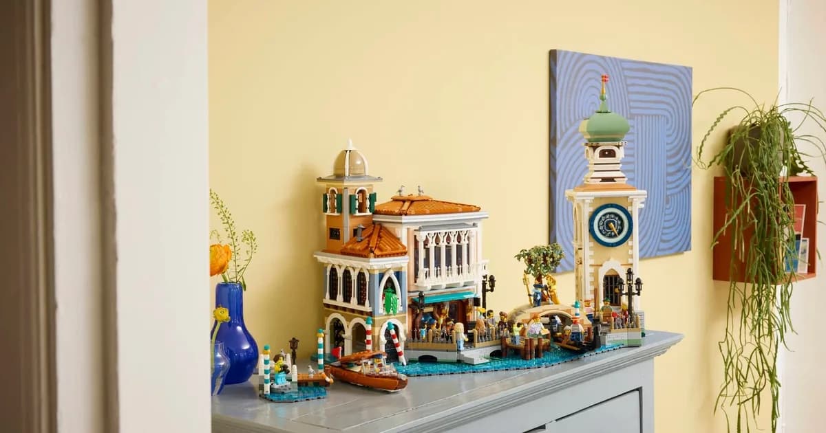 LEGO Venetian Neighborhood on a grey cabinet against a yellow wall, green onion-domed clock tower on the right, water taxi in front