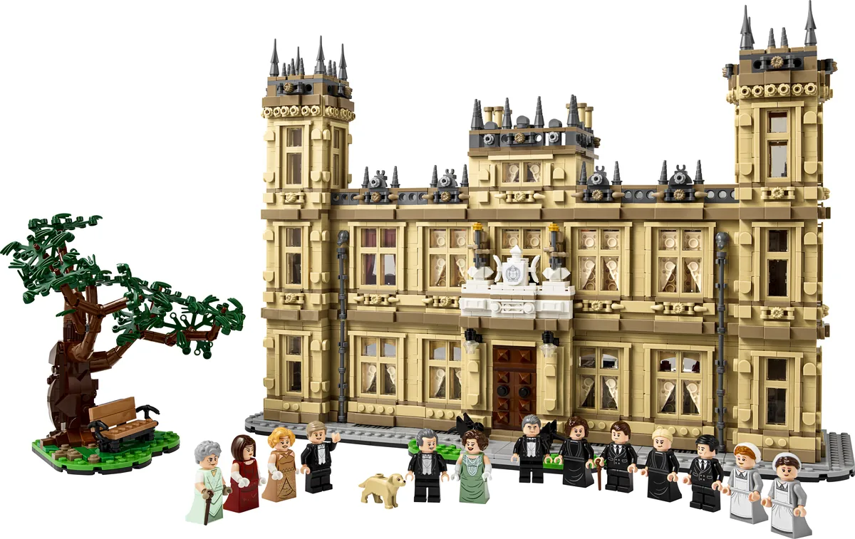LEGO Ideas Downton Abbey 21373, a tan stately house with towers, a tree with a bench beside it and a row of minifigures in front