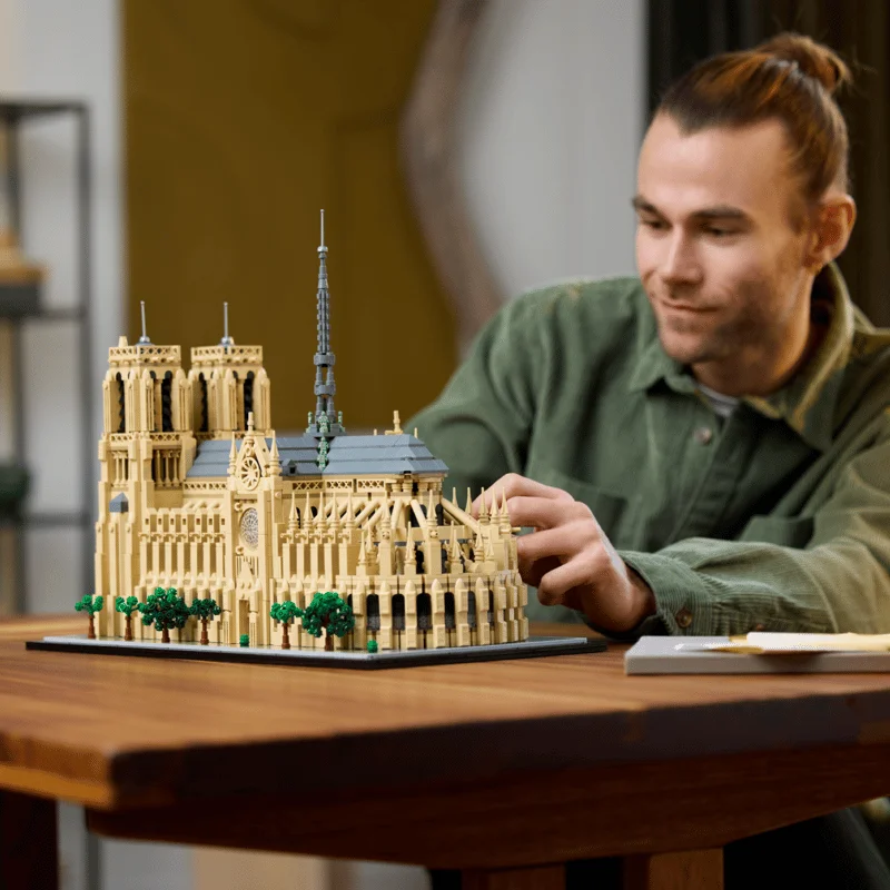 LEGO Architecture Notre-Dame de Paris model on a wooden table, a man in a green shirt adding pieces to the nave