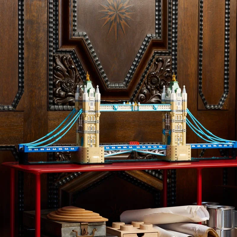 LEGO Architecture Tower Bridge model with blue suspension cables and twin stone towers on a red table in front of carved wooden panels