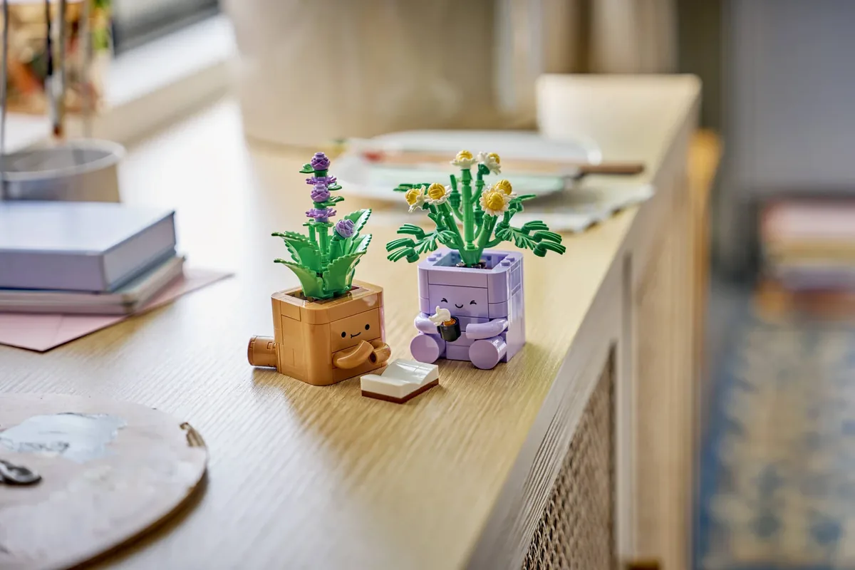 LEGO Cozy Plants on a light wooden sideboard next to a stack of books and a plate, the peppermint in its brown pot and the chamomile in its purple pot