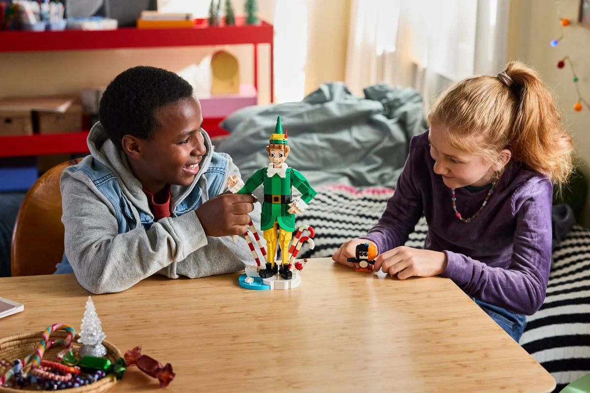 Two children at a table with the finished LEGO Buddy the Elf figure and a pile of candy canes