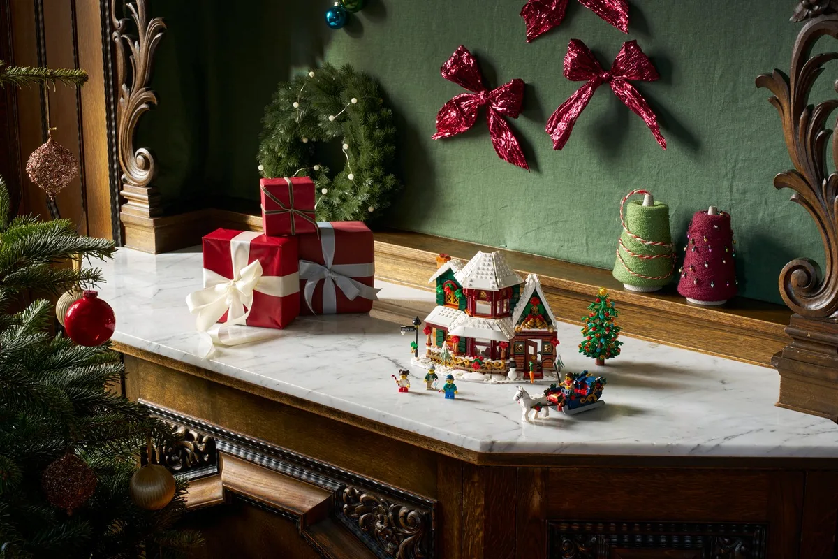 The LEGO Holiday House with its sleigh and a small Christmas tree on a marble mantel, beside wrapped gifts and red bows