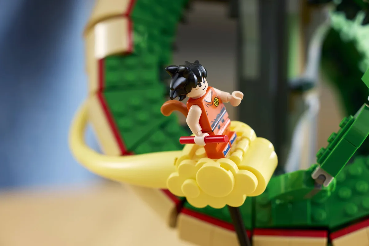 Close-up of the Kid Goku minifigure in an orange outfit sitting on the yellow Kintoun cloud, green dragon scales behind him
