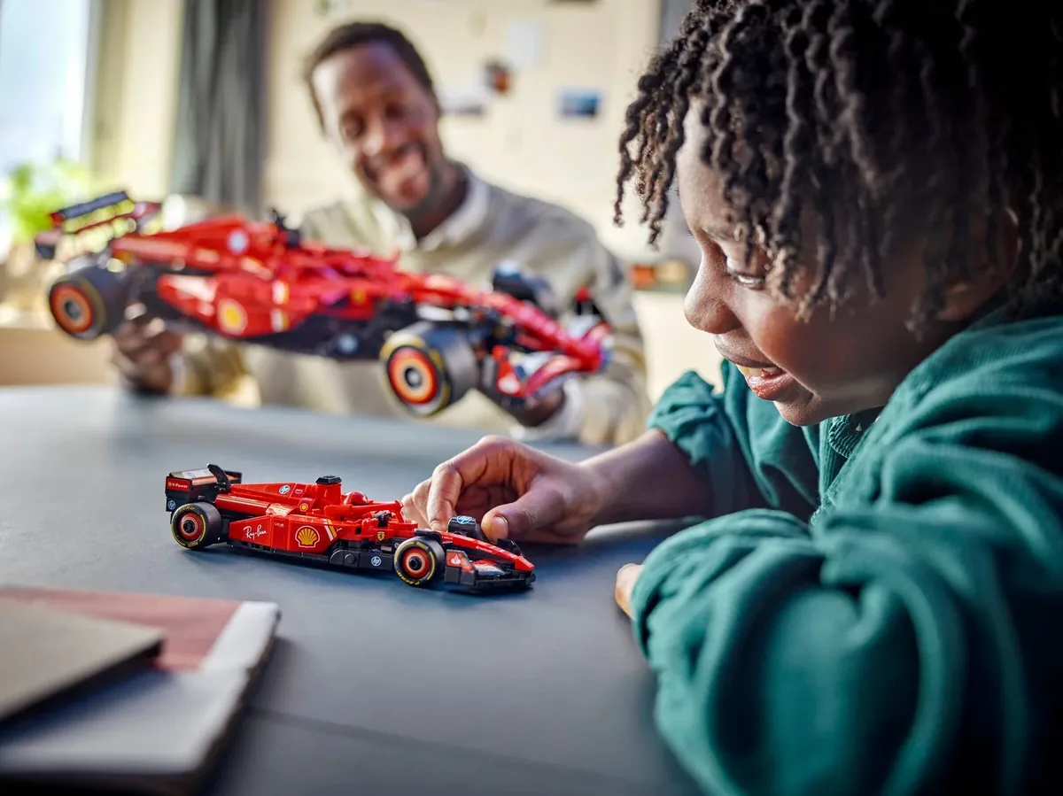 LEGO Technic Ferrari SF-24 F1 car held by an adult while a child pushes the small Speed Champions Ferrari across a table