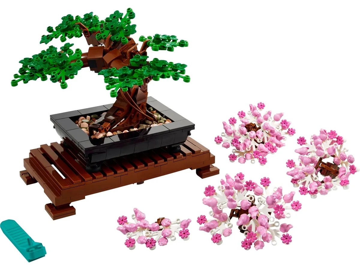 LEGO Icons Bonsai Tree 10281 in a black pot on a brown wooden stand, with pink blossom pieces laid out beside it