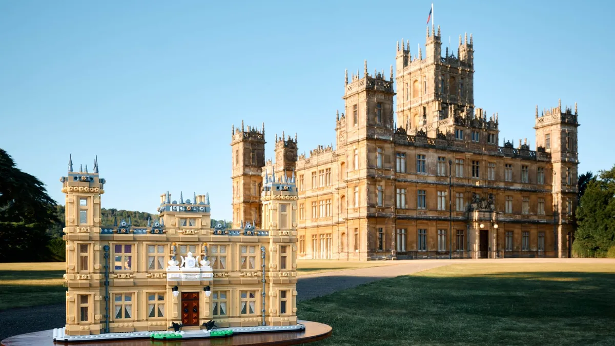 LEGO Ideas Downton Abbey 21373 on a round display base on the lawn in front of the real Highclere Castle