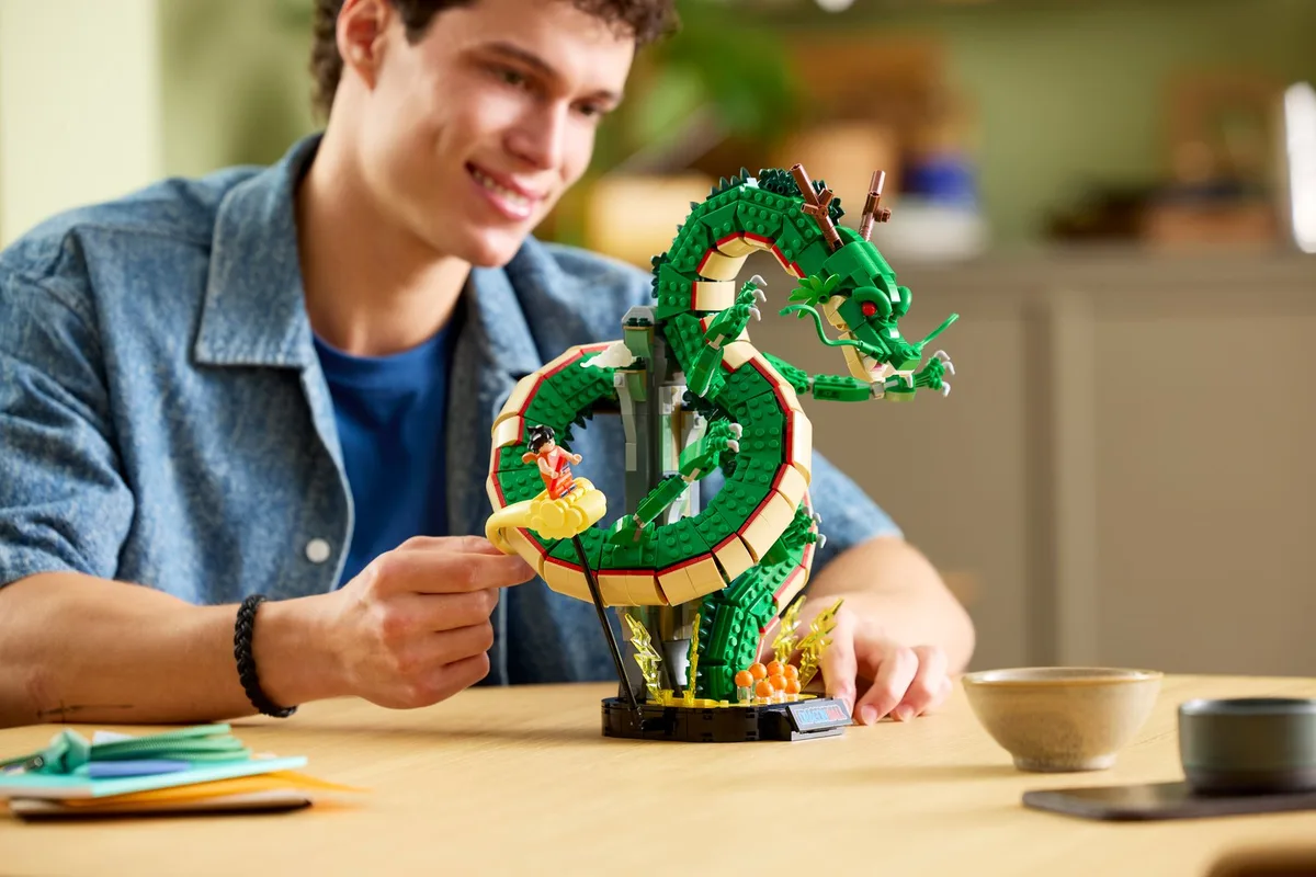 A man at a table building the green LEGO Shenron dragon, with the Goku minifigure on the Kintoun cloud