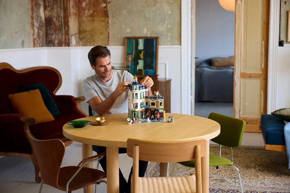 A man building LEGO Icons Shopping Street 11371 at a round wooden table in a room with armchairs