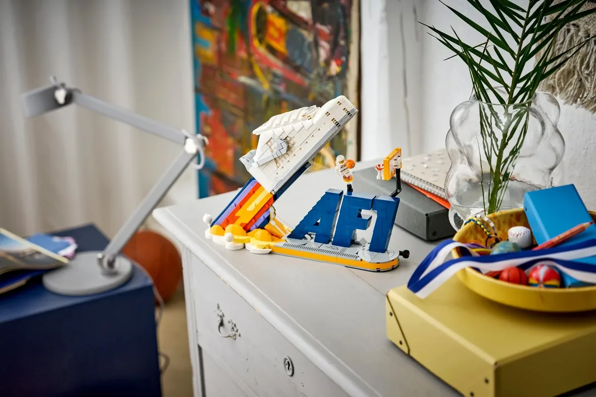 LEGO Nike Air Force 1 sneaker built as a white rocket over blue AF1 letters on a dresser beside a desk lamp