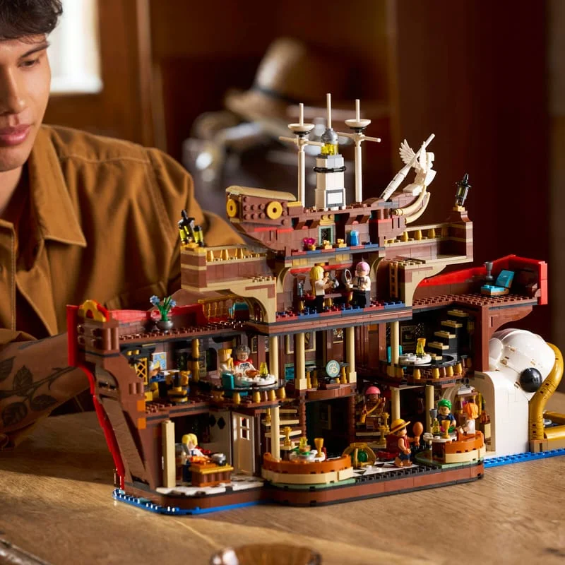 LEGO ONE PIECE Baratie floating restaurant built on a wooden table, several decks with minifigures, a builder in a brown jacket behind it