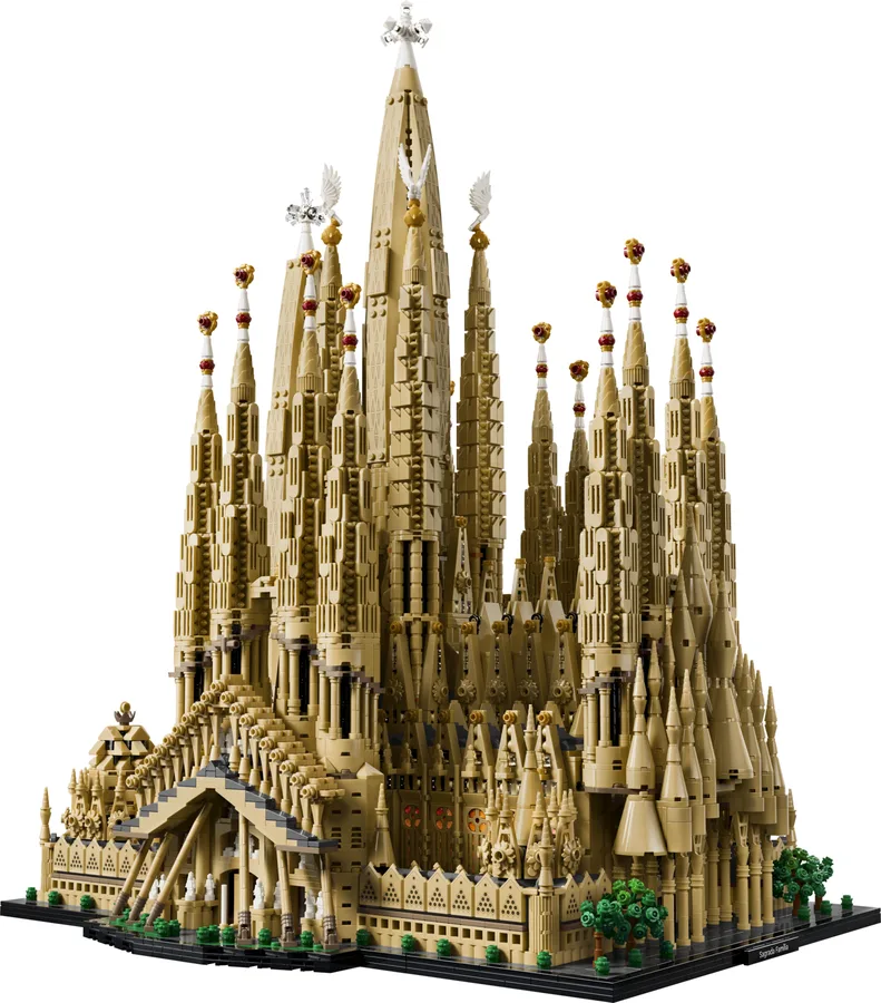 The complete LEGO Sagrada Família model from a three-quarter angle, its tall central spire and clustered towers above a dark base with small trees