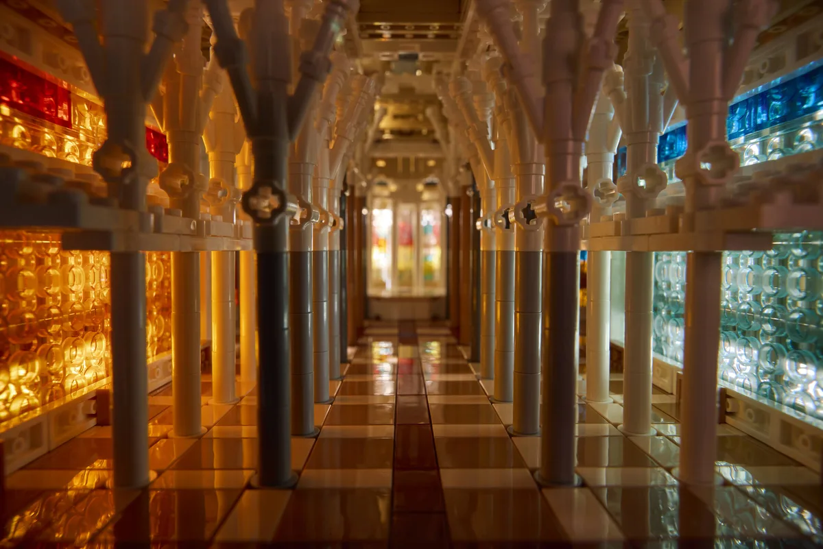 Looking down the nave of the LEGO Sagrada Família model, branching tan columns lined with red, amber, blue and teal glass panels
