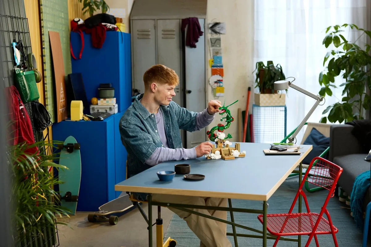 LEGO Rayquaza 72168: a man at a blue table posing the finished Rayquaza, with lockers and a skateboard behind him