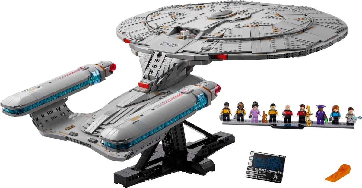 LEGO Star Trek Enterprise-D 10356 on its black stand on white, nine crew minifigures on a display tile beside the name plaque