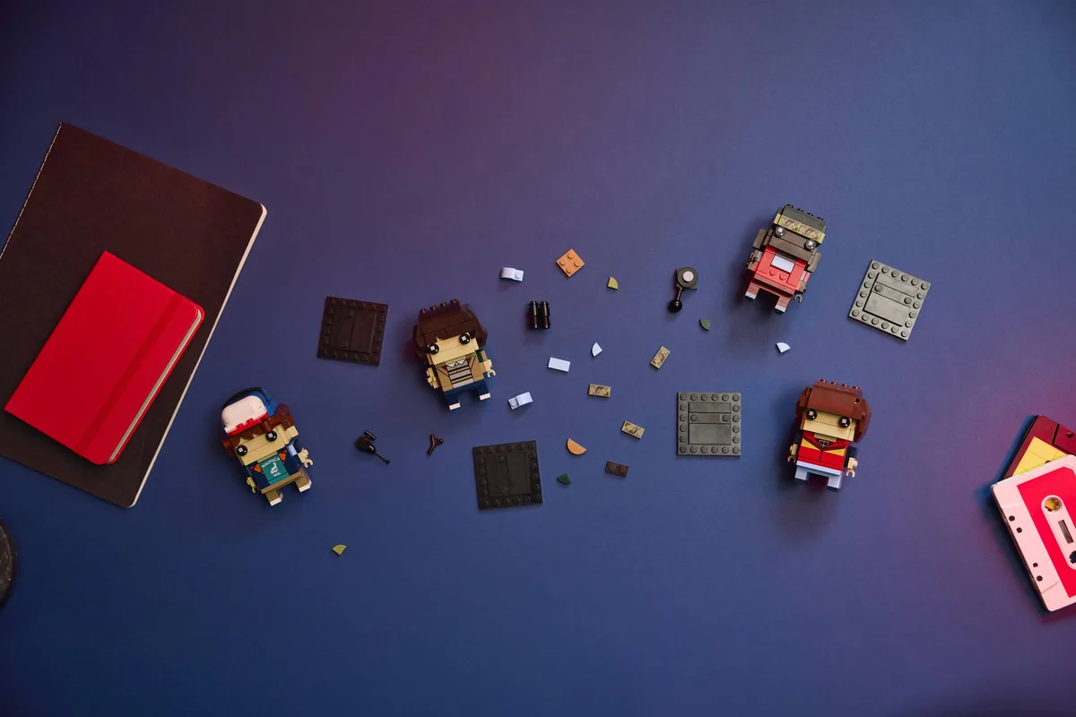 LEGO BrickHeadz 40801 Mike, Dustin, Lucas and Will part-built on a purple-blue surface beside a red notebook and a cassette