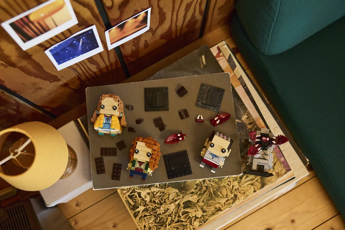 LEGO BrickHeadz 40879 Eleven, Max, Holly and the Demogorgon with loose pieces on a wooden shelf, photos pinned above