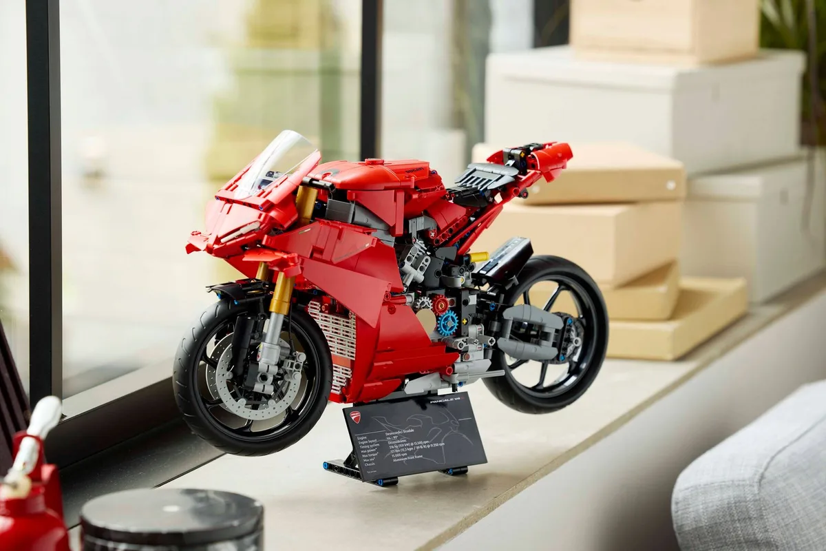 The red LEGO Technic Ducati Panigale V4 S motorcycle on its black stand with the printed spec plate, on a window sill