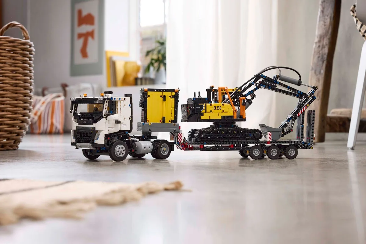 The finished LEGO Technic Volvo FMX truck towing a low loader with the yellow Volvo EC230 excavator on it, on a concrete floor