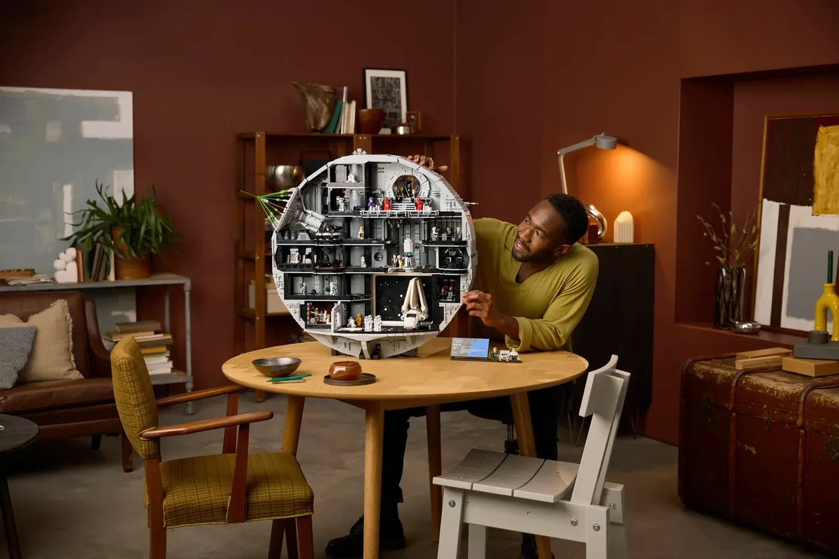 A man at a round wooden table holding up the round grey LEGO Star Wars Death Star 75419, cut open to show its rooms