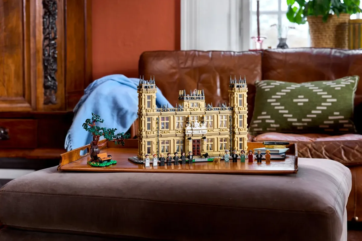 The LEGO Ideas Downton Abbey 21373, a tan country house model with minifigures, on a tray on an ottoman in front of a leather sofa
