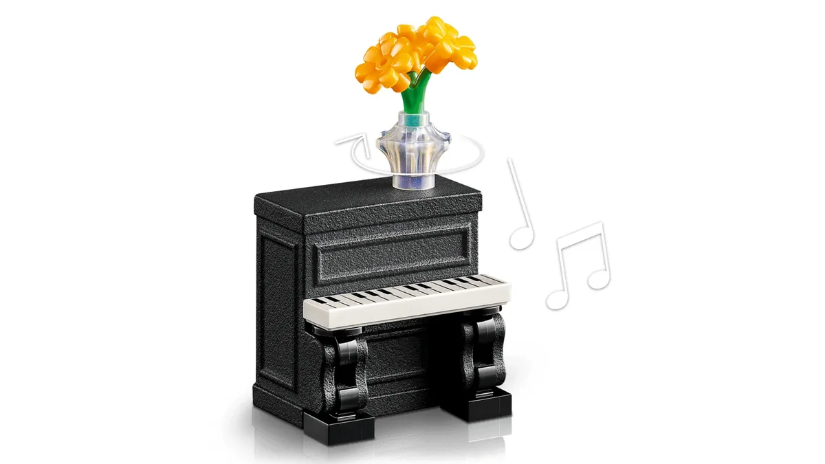 Close-up of the black 3D-printed LEGO street piano with white keys and a vase of orange flowers on top, with an arrow showing the vase turns
