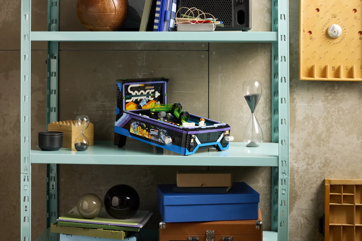The purple and blue LEGO Arcade Pinball Machine model on a pale green metal shelf beside boxes and an hourglass