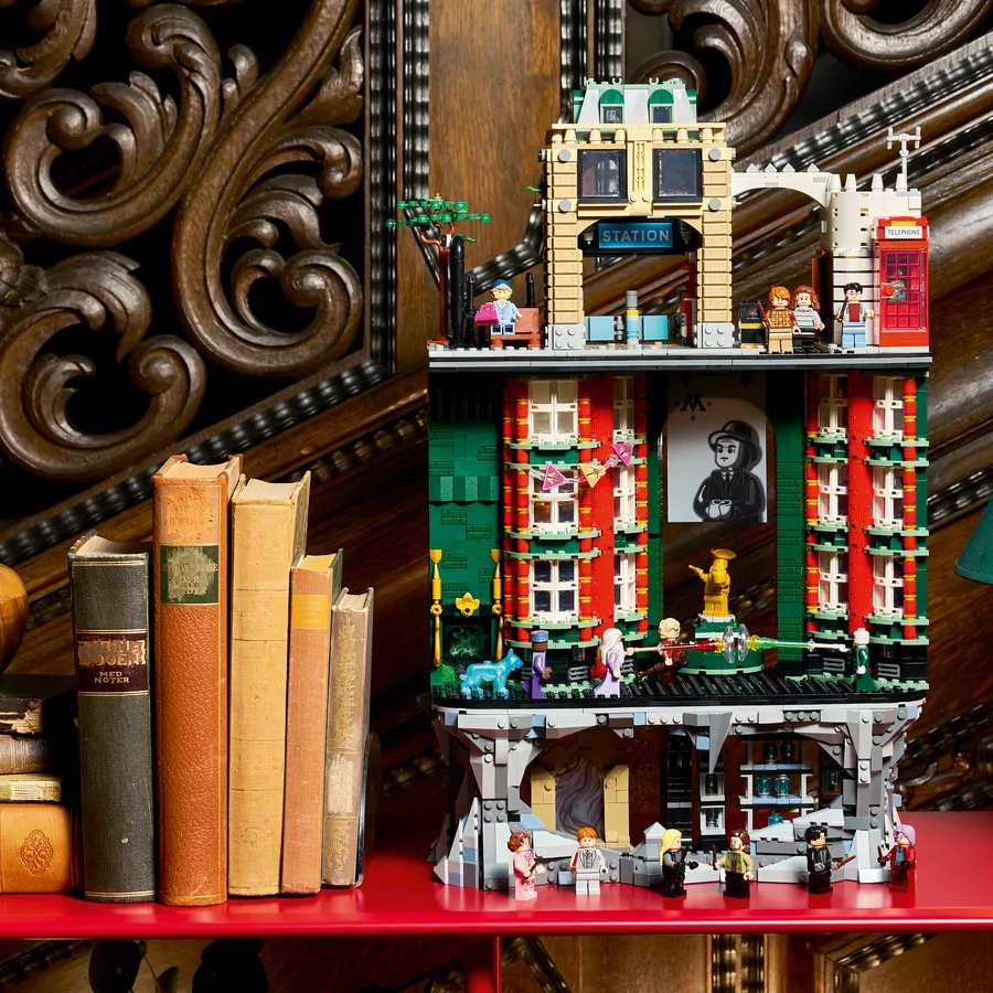 The tall green and red LEGO Ministry of Magic building, with minifigures on several floors, beside a row of old books
